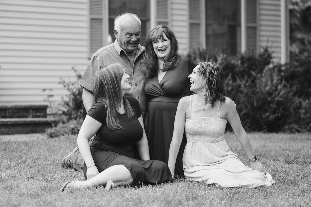 Black and white portrait of three people relaxing together on the lawn in front of a house.