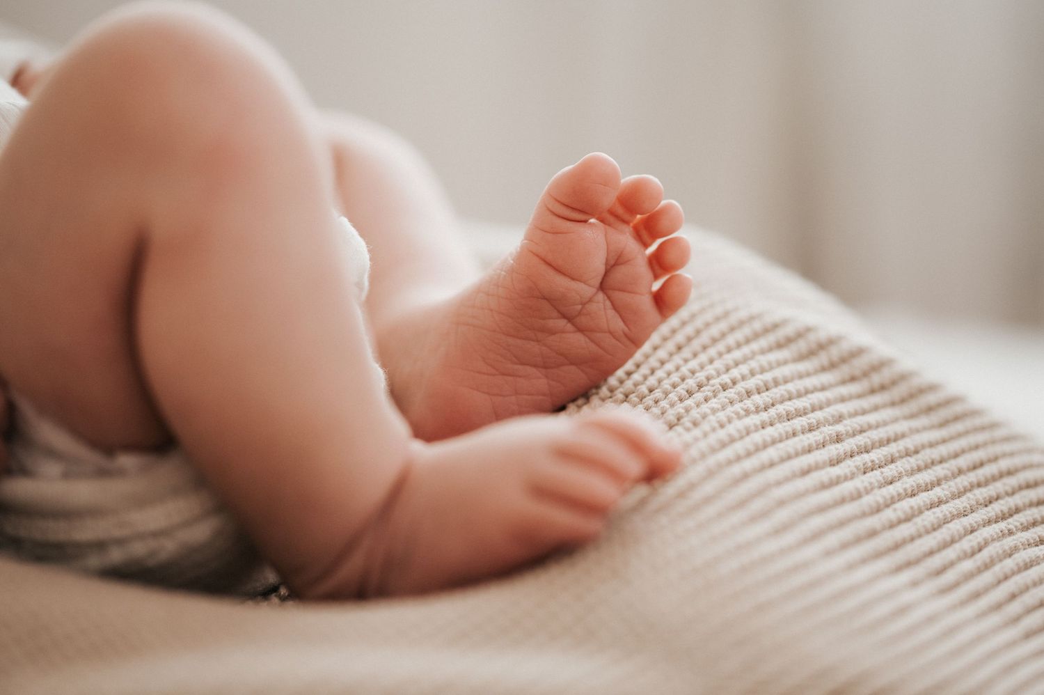 Tiny newborn baby feet rest on soft white knitted fabric in natural window light.