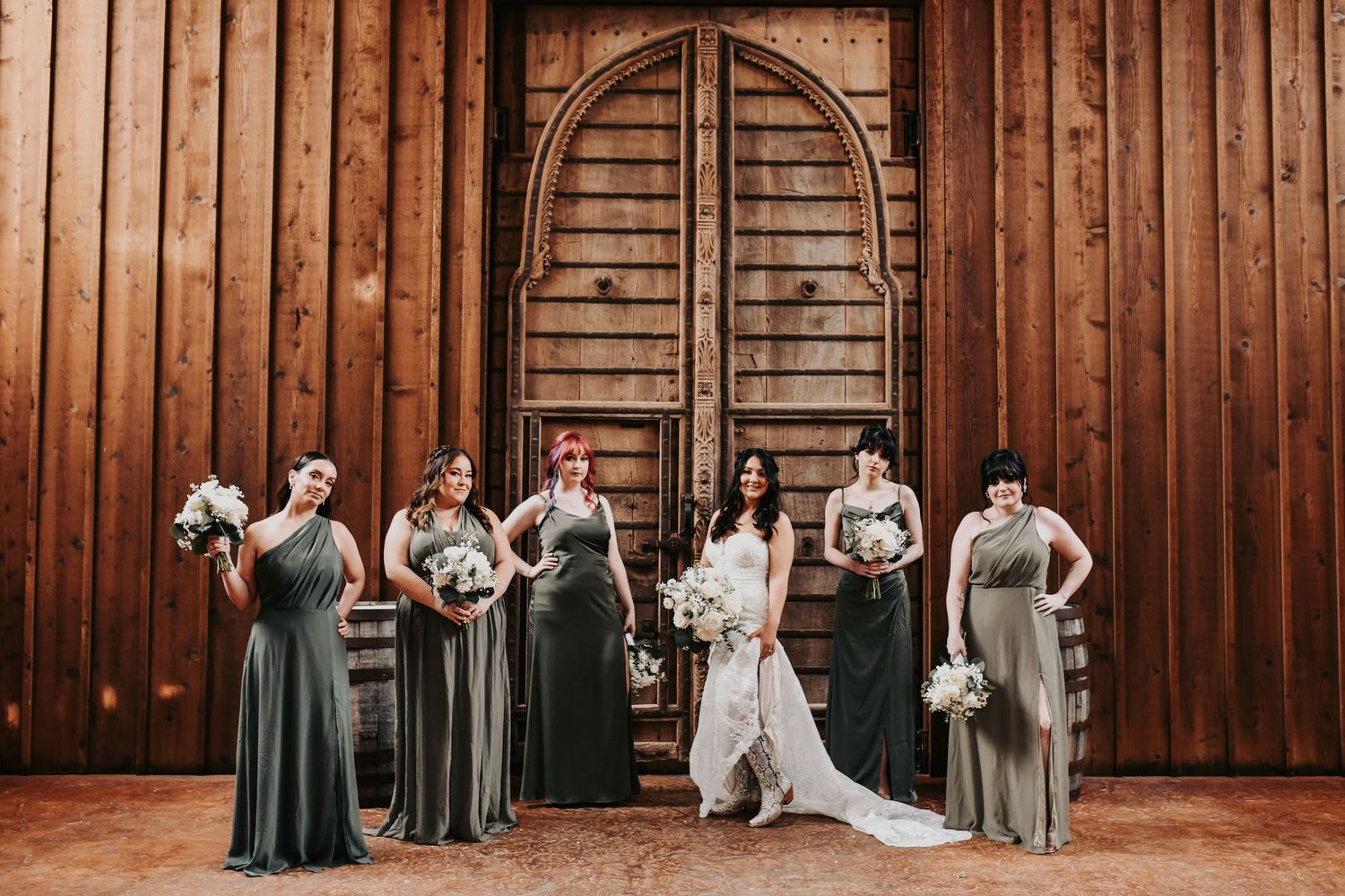 Bridesmaids in sage gowns with loose greenery bouquets standing beside the bride for a modern editorial look.