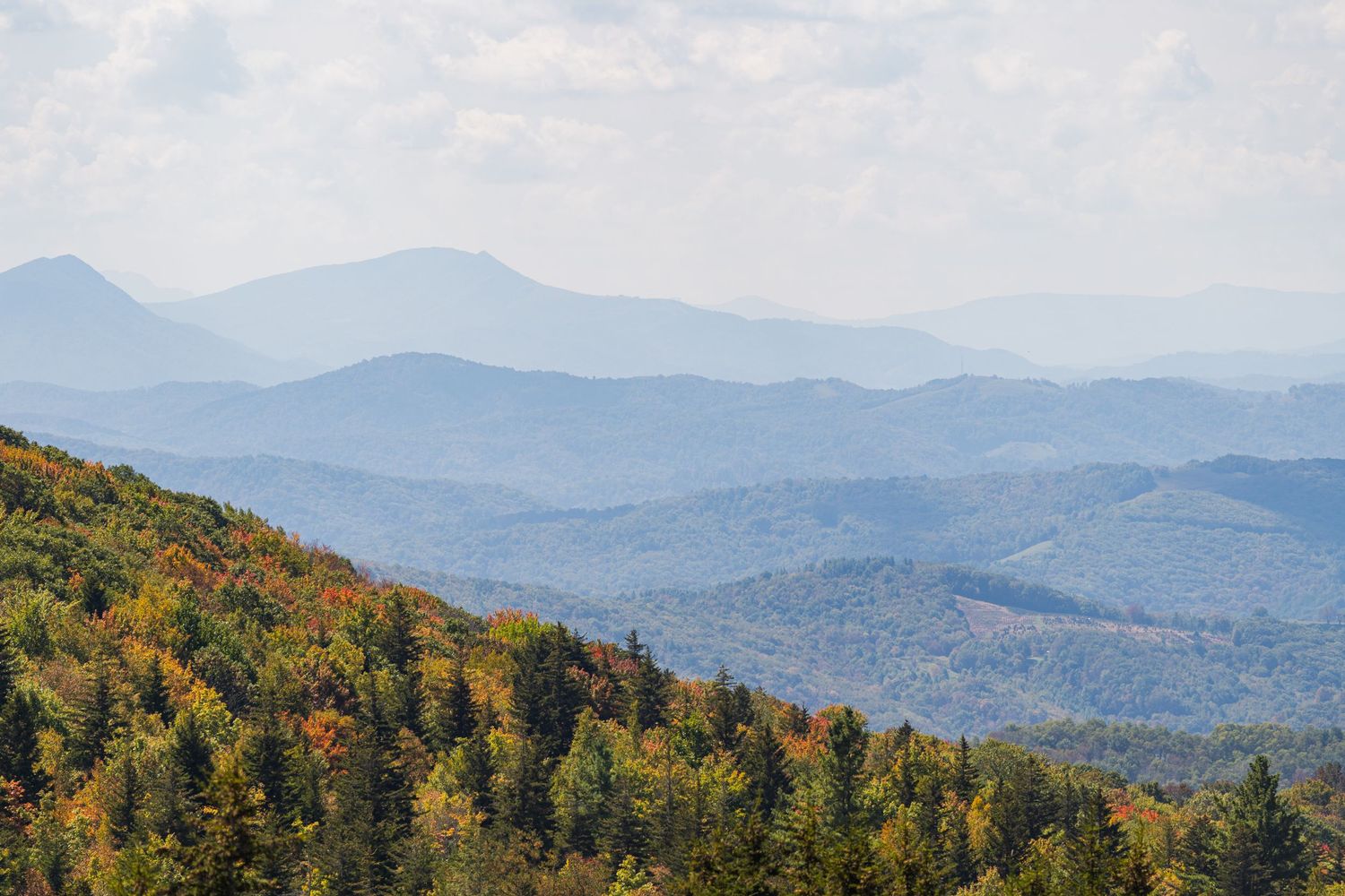 Mountain ridges covered in autumn foliage stretch into the distance under a hazy blue sky in the Appalachian range.