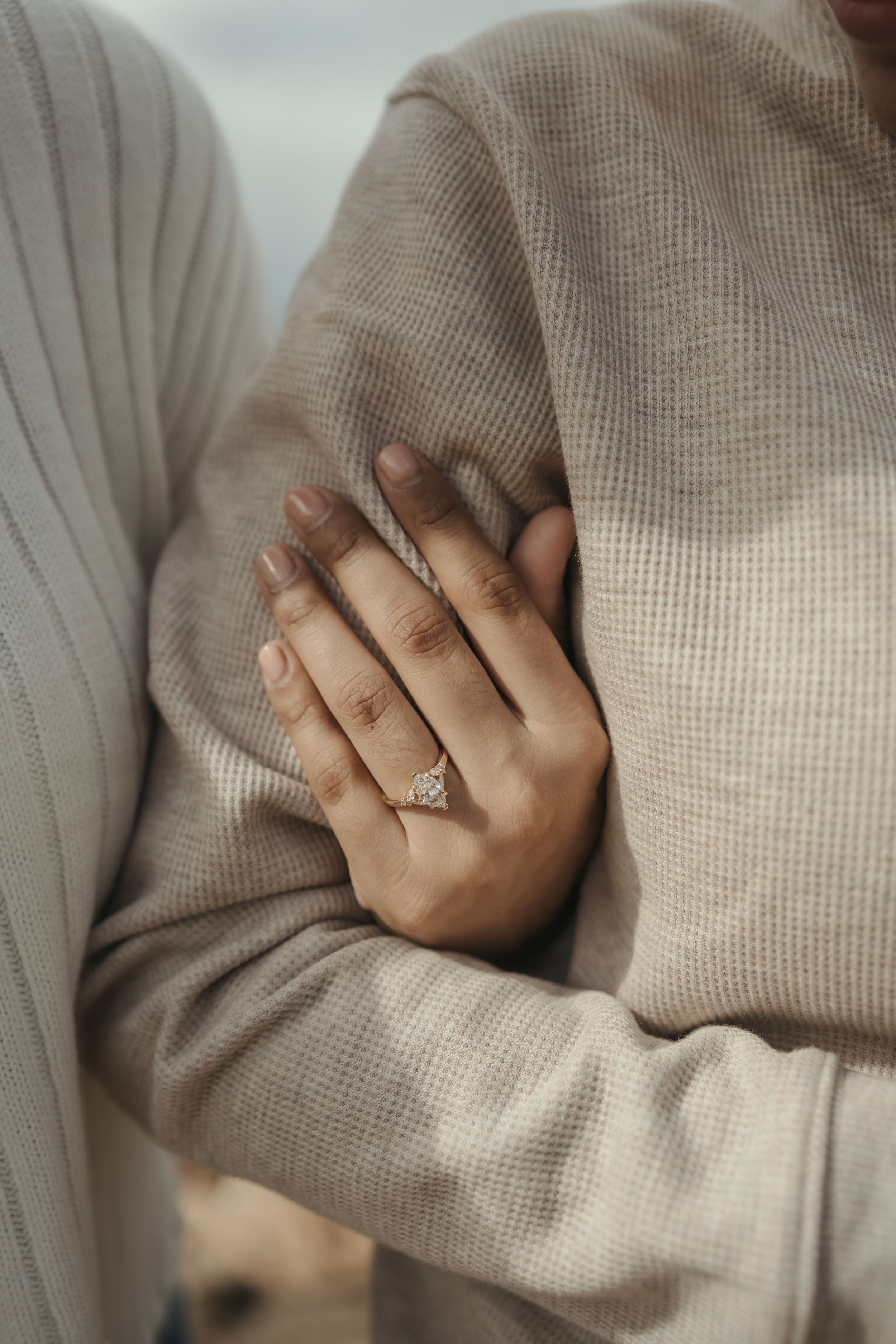 Close-up view of a diamond engagement ring on a hand resting against a soft beige knit sweater.