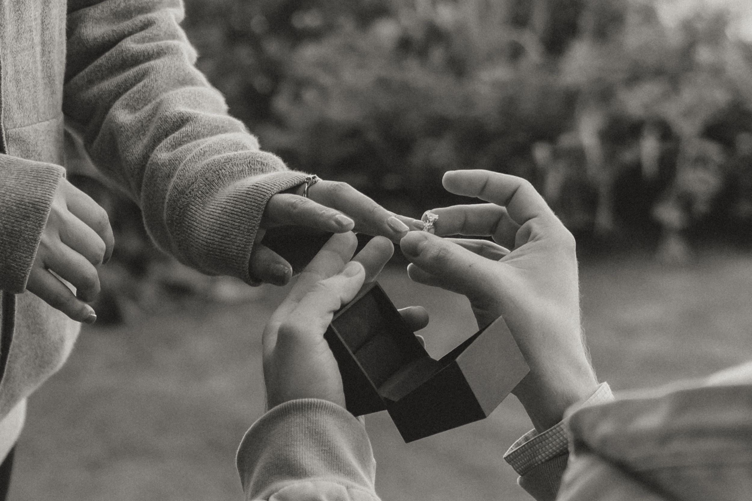 Two pairs of hands exchanging a small black object outdoors in a black and white photograph.