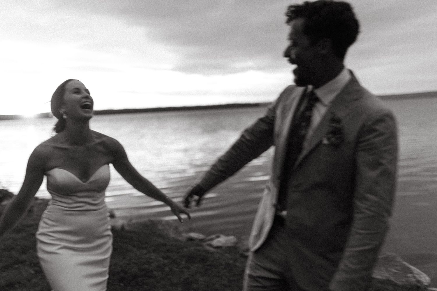Black and white photo of a couple laughing together on a beach during their wedding celebration.