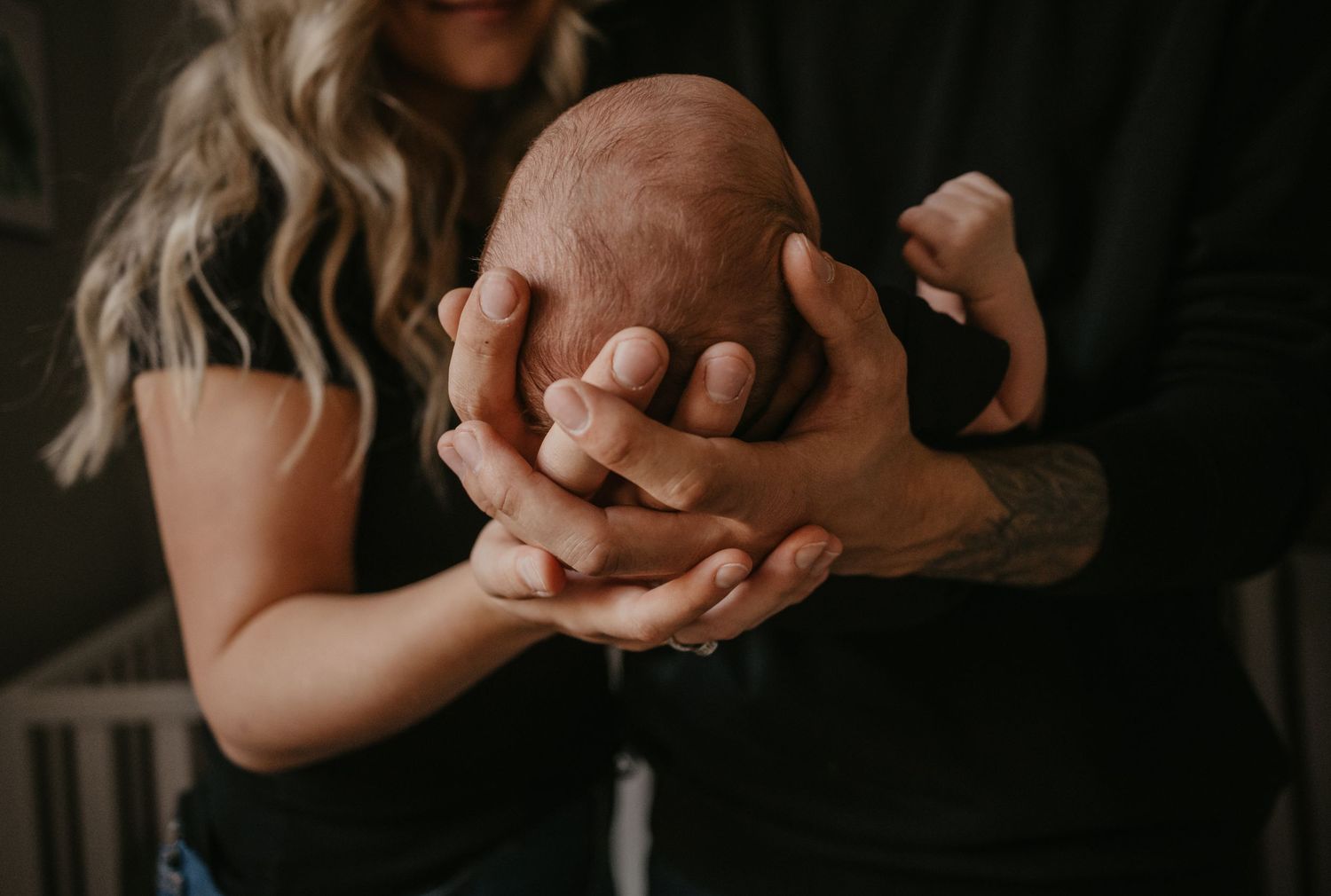 Two pairs of hands gently hold each other in a tender moment against a dark background.