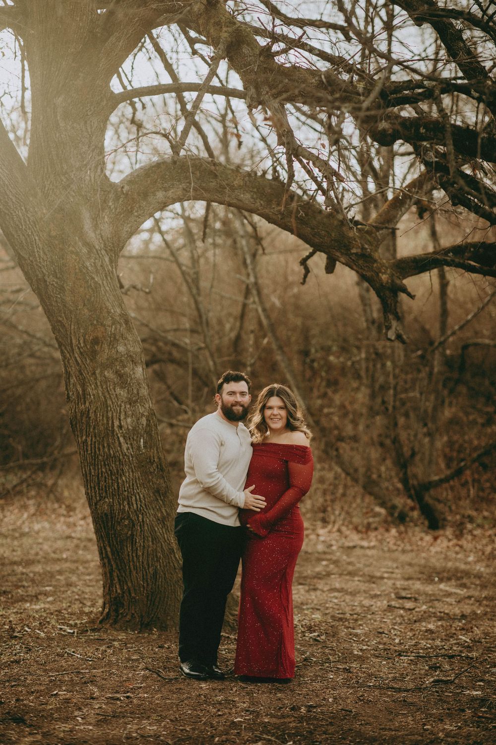 A couple embraces under autumn trees in a romantic outdoor photoshoot with warm sepia tones.