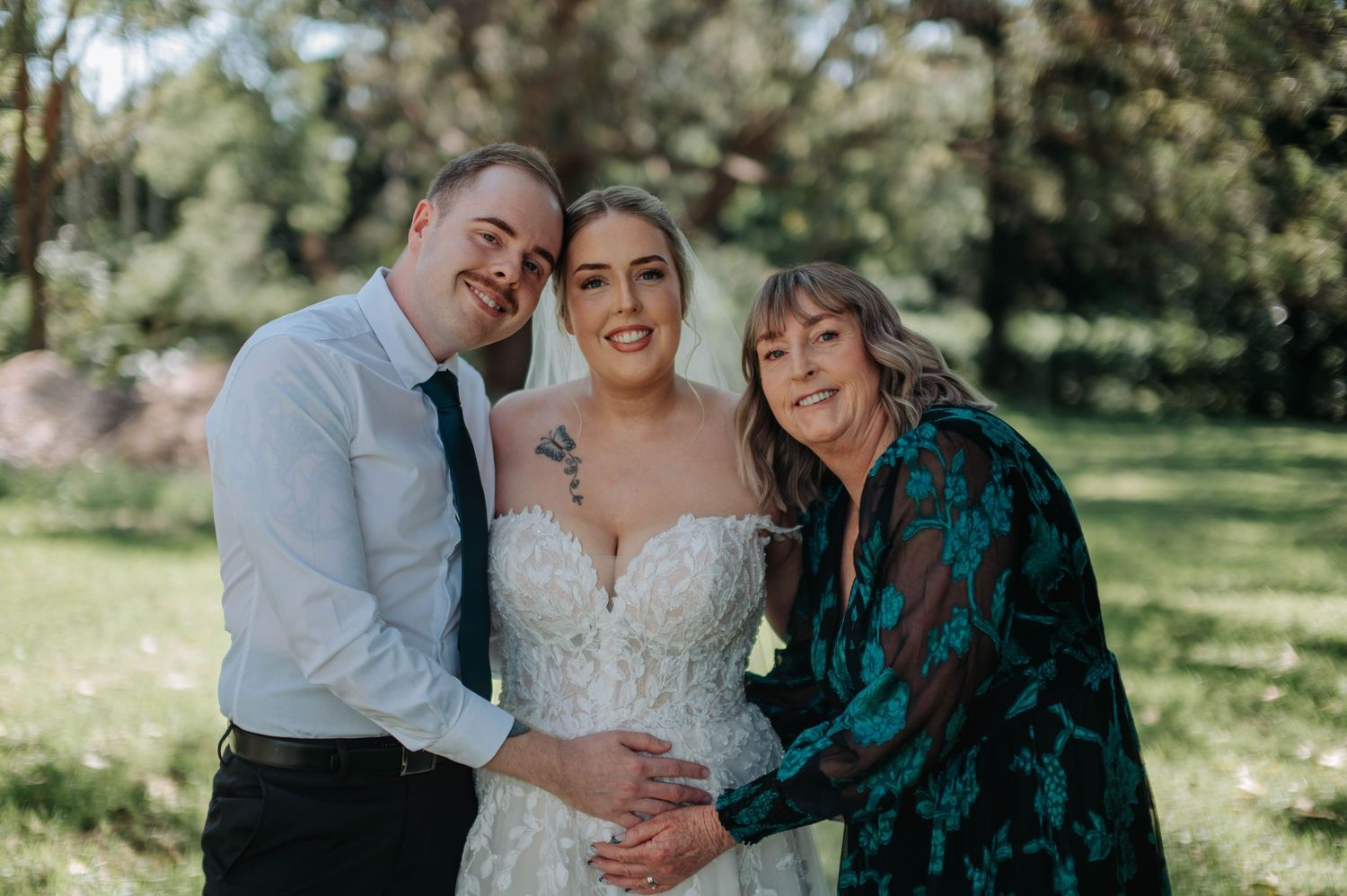 A couple and an older woman share joyful moments together in a sunny outdoor garden setting.