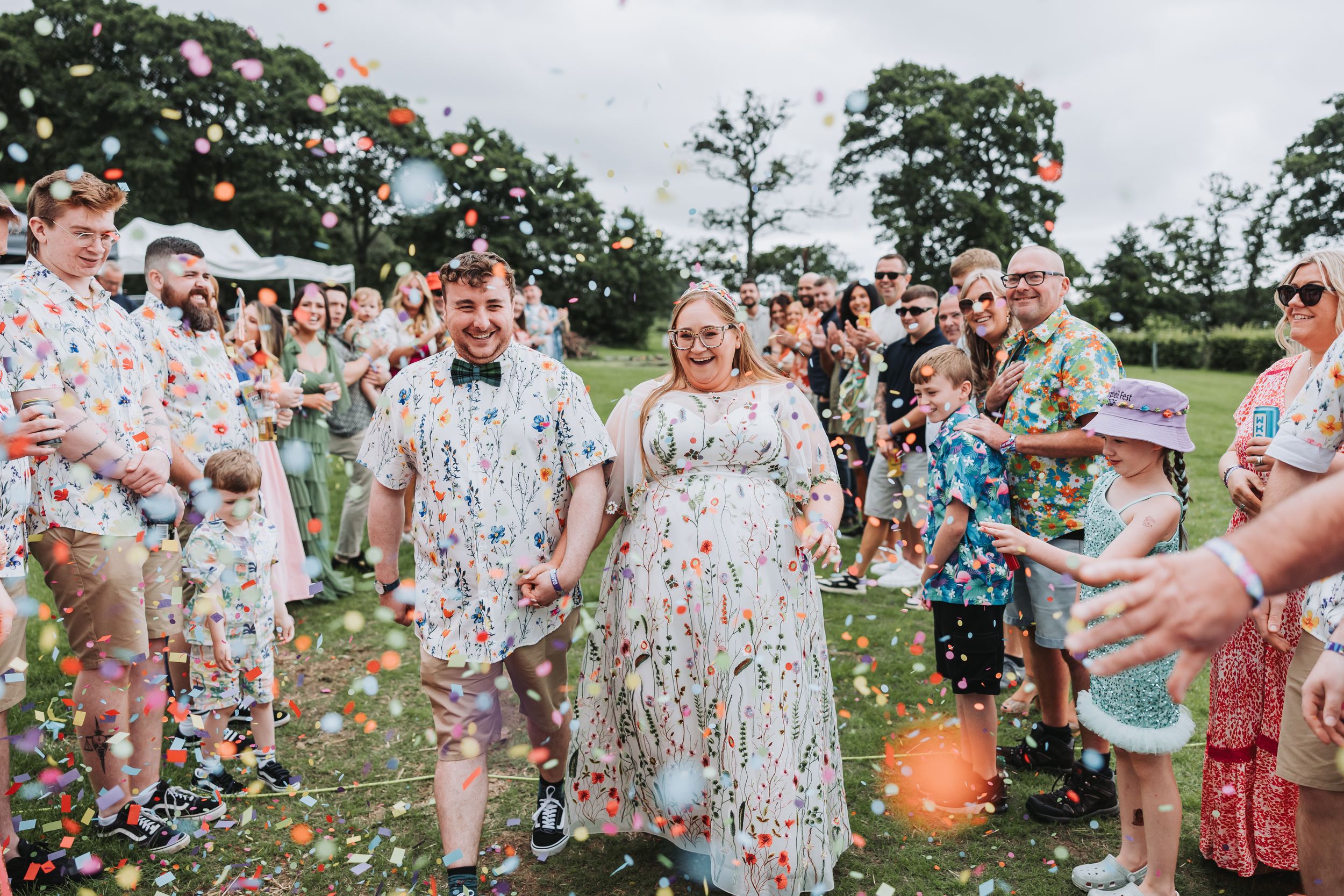 Wedding guests celebrate with colorful confetti toss outdoors on a sunny day.