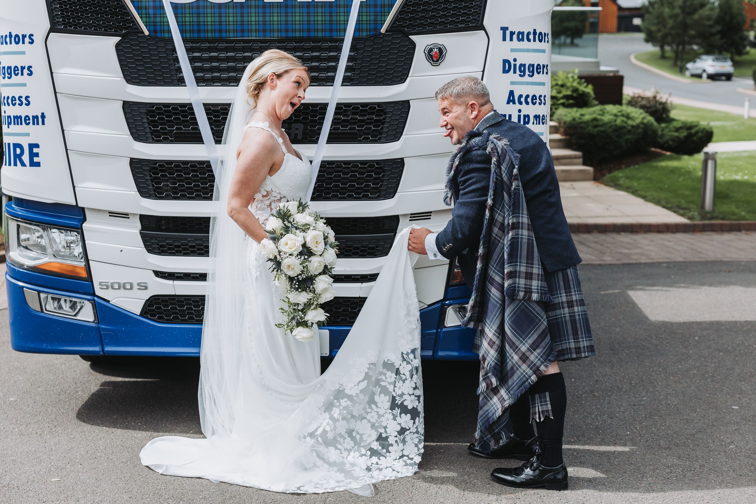 A bride in a white wedding dress poses in front of an HGV