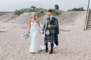 Wedding couple walking along a sandy beach path with scenic coastal views.