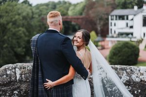 Couple embracing on stone bridge with scenic countryside views.