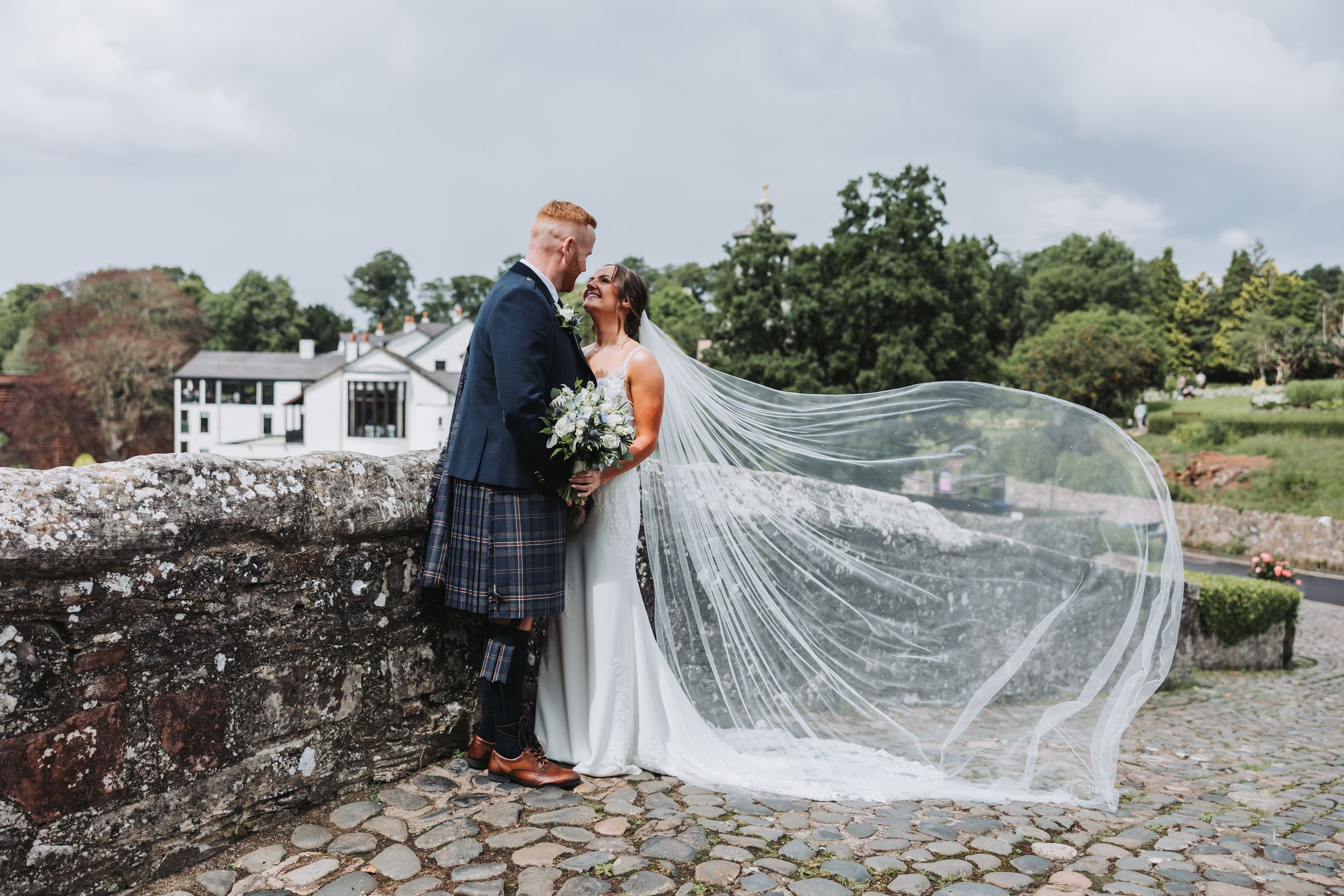 Long flowing veil catches wind against stone wall backdrop.