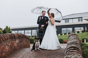 Couple poses on stone wall with umbrella against cloudy sky.