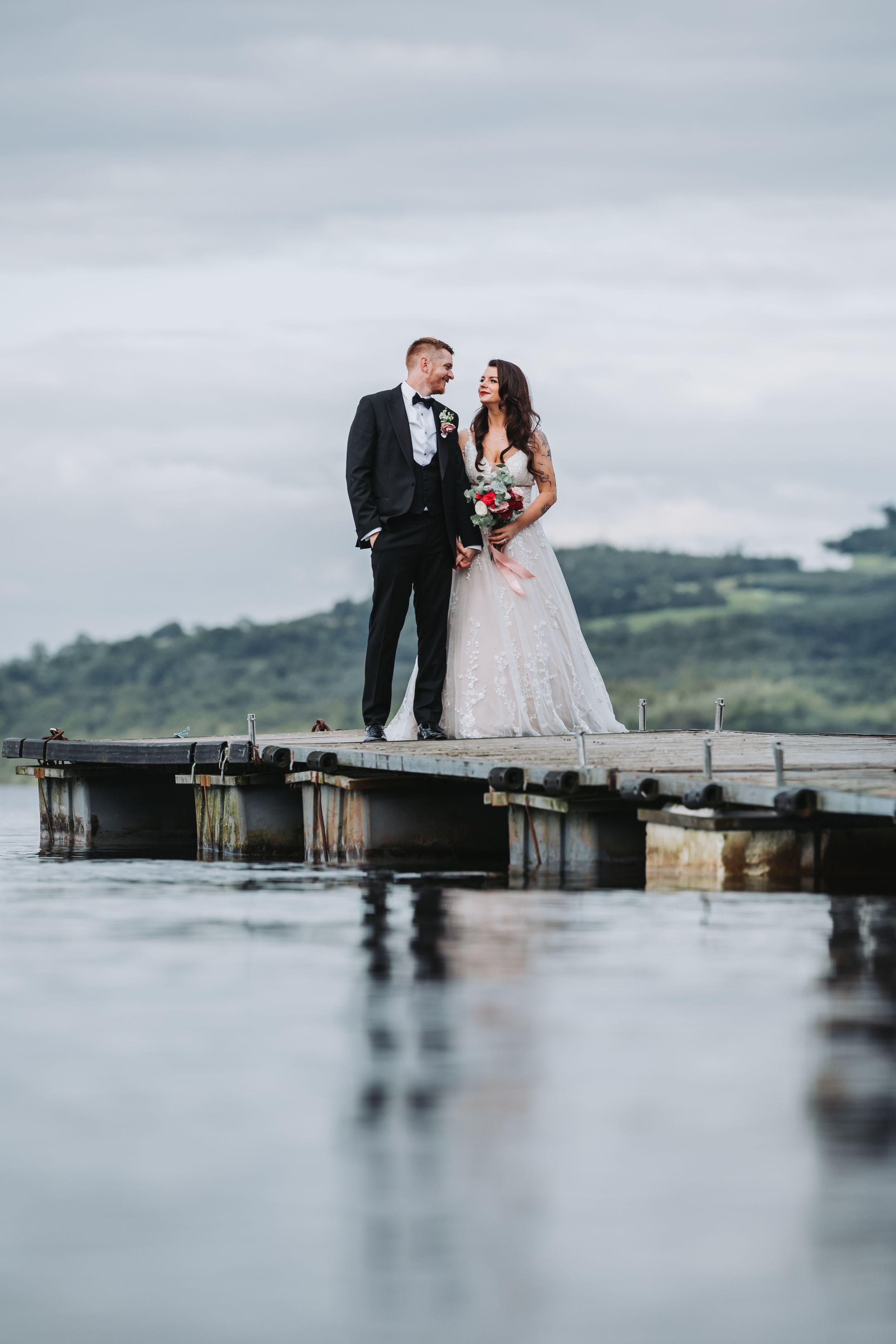 Couple stands on wooden pier overlooking misty lake landscape.