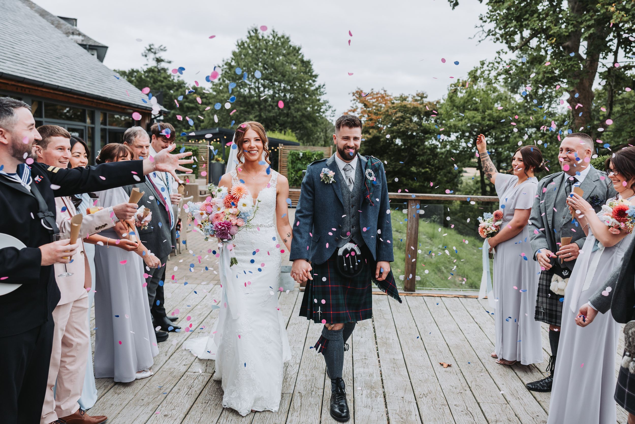 Wedding celebration on a wooden deck with guests throwing confetti in celebration.