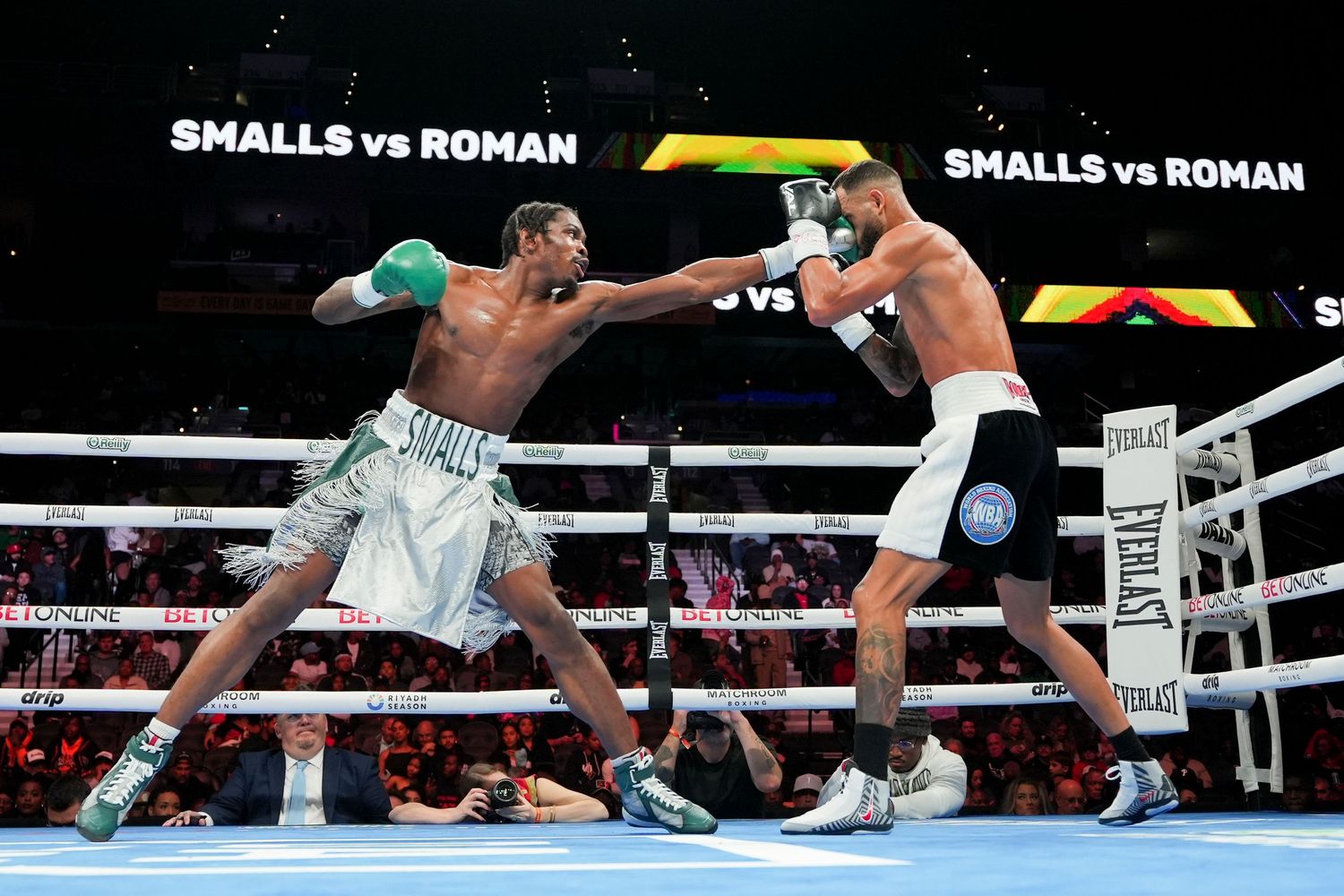 Two boxers exchange punches during the Smalls vs Roman professional boxing match in a packed arena.