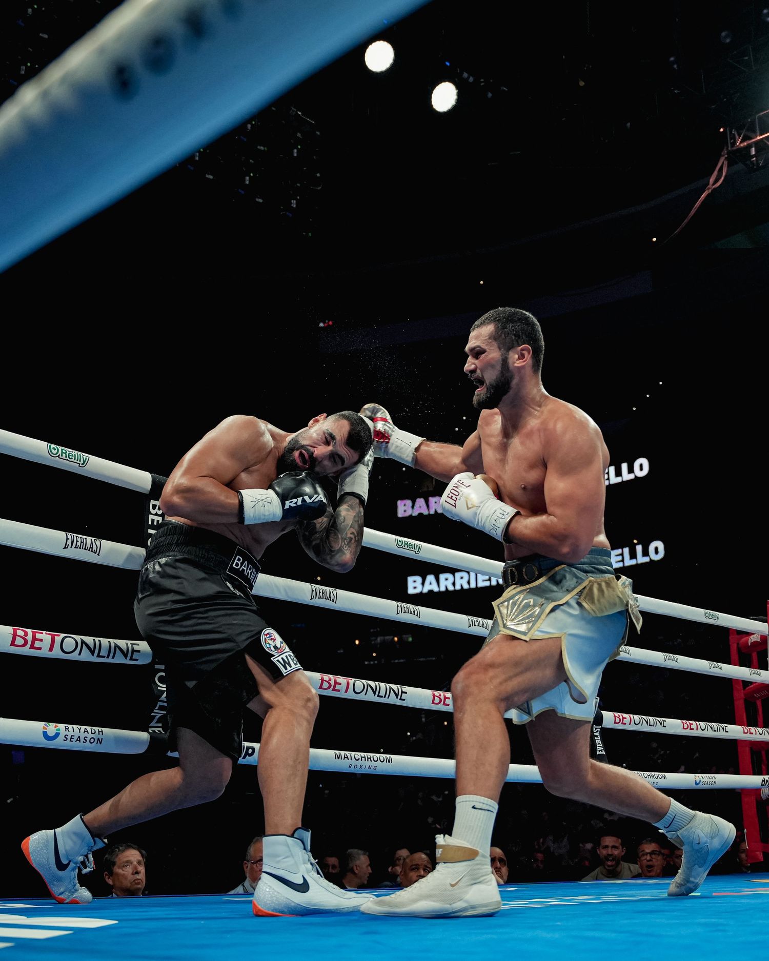 A shirtless boxer lands a powerful right hook on his opponent during the Barrios vs Costello bout.