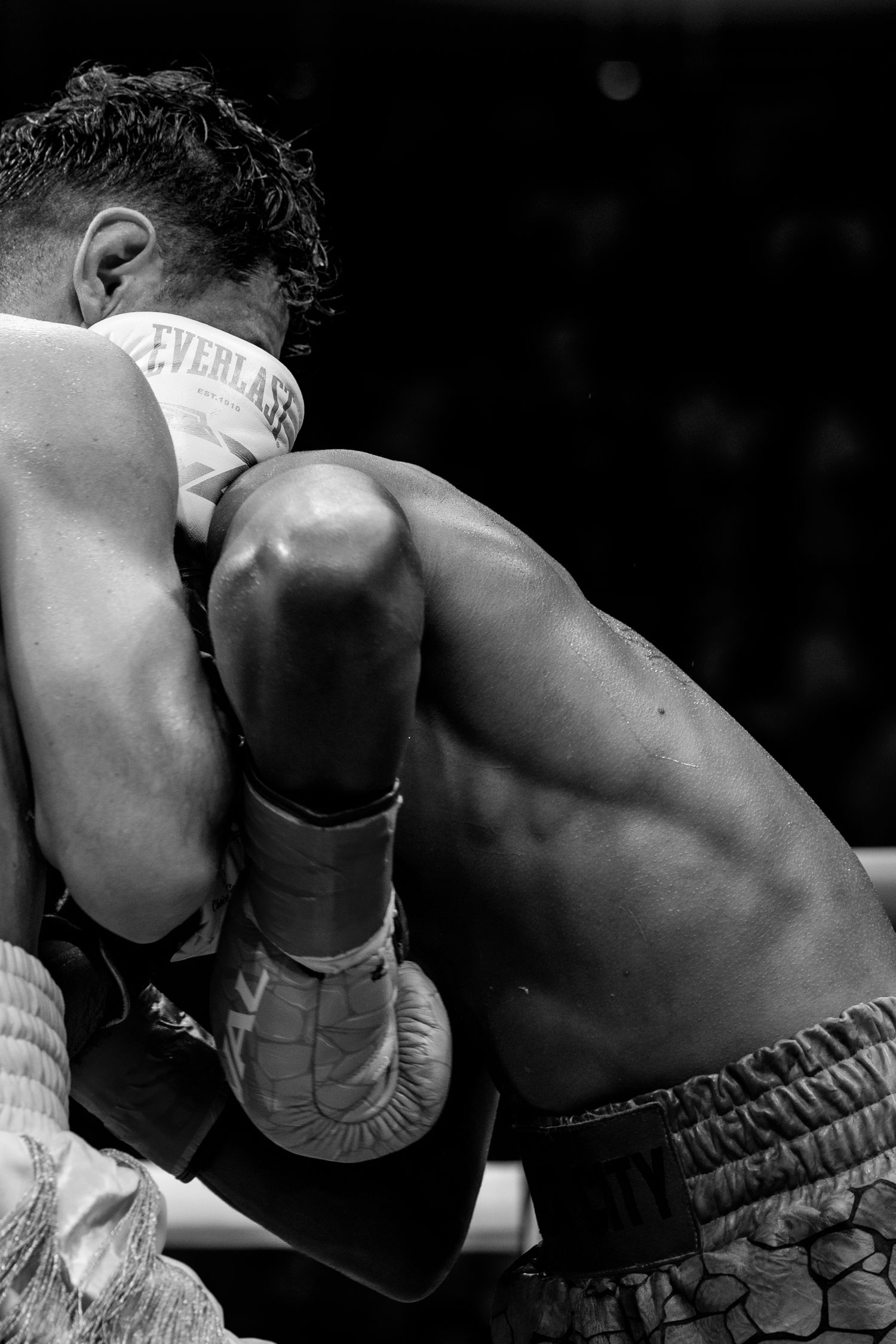 Two boxers clinch in an intense black and white close-up shot during a professional boxing match.