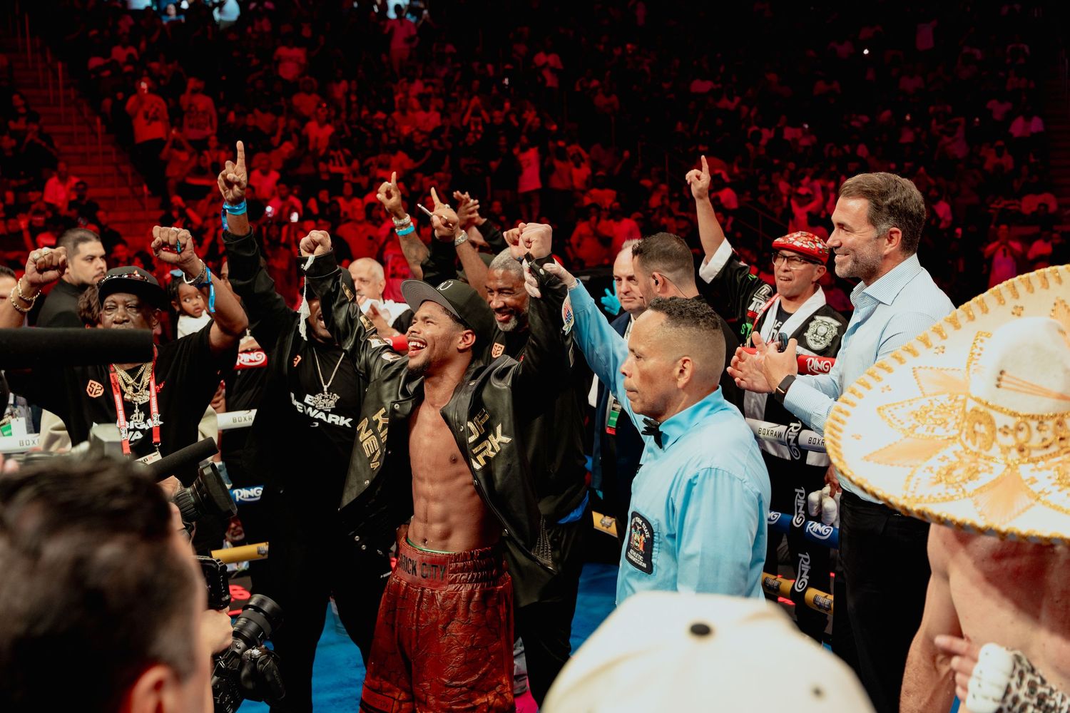 A victorious boxer celebrates with his team in the ring after winning a professional boxing match.