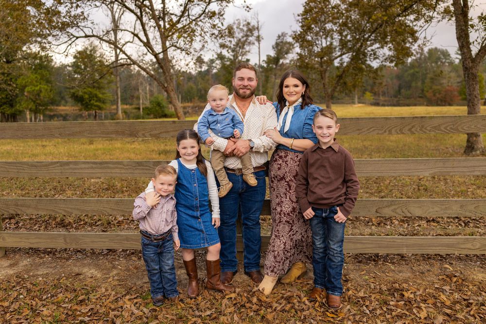 Family group portrait taken outdoors in autumn setting with fallen leaves.