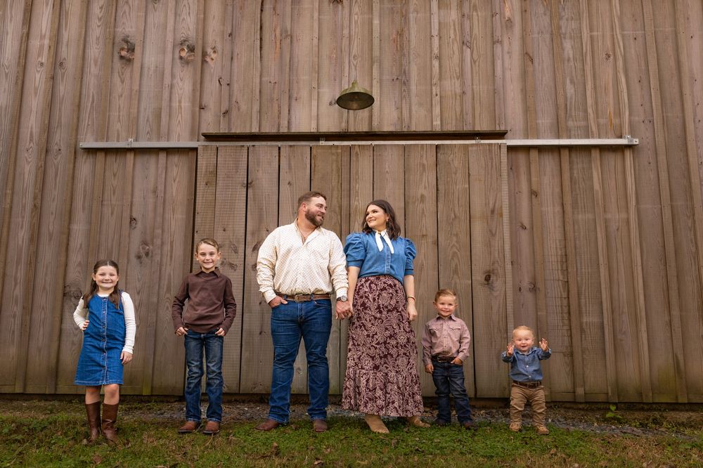 Family poses together in front of wooden fence during outdoor photo session.