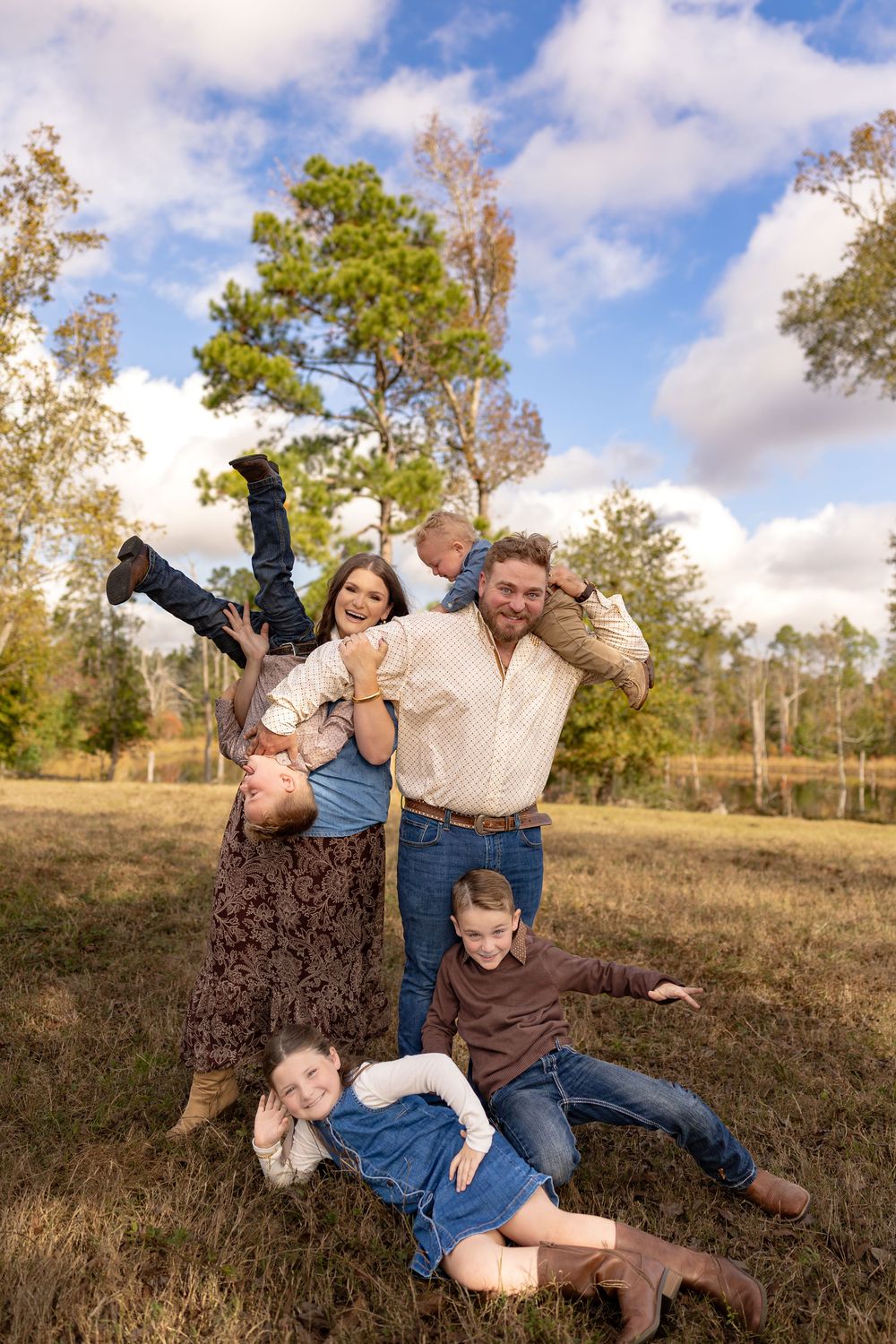 Family plays and laughs together while lying in grass under blue sky.