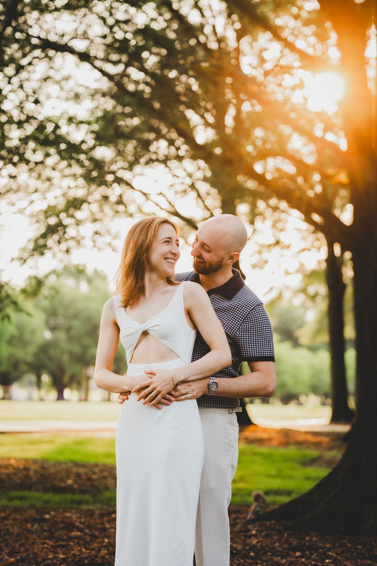 A couple shares tender moments in a park at sunset with golden sunlight filtering through trees.