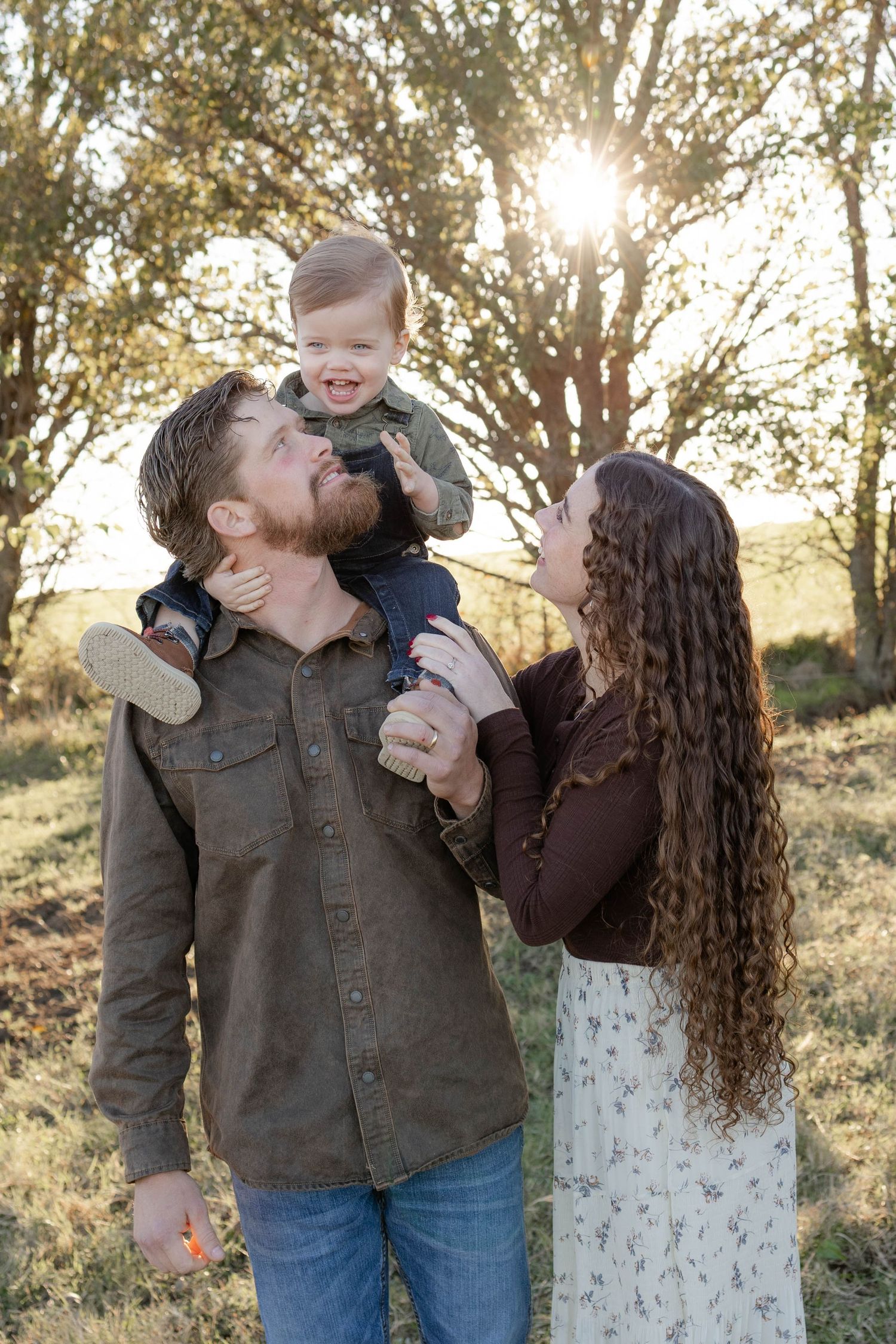A couple poses together in a golden field at sunset during a fall outdoor photo session.