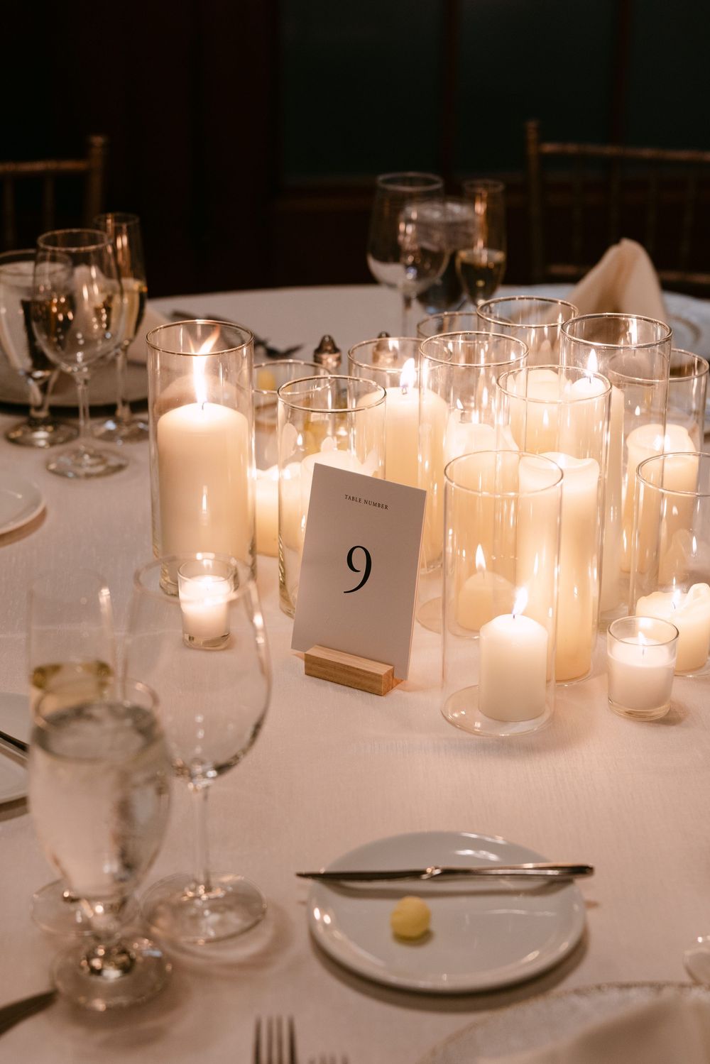 White candles in glass holders illuminate an elegant table setting with place numbers at a formal dinner event.