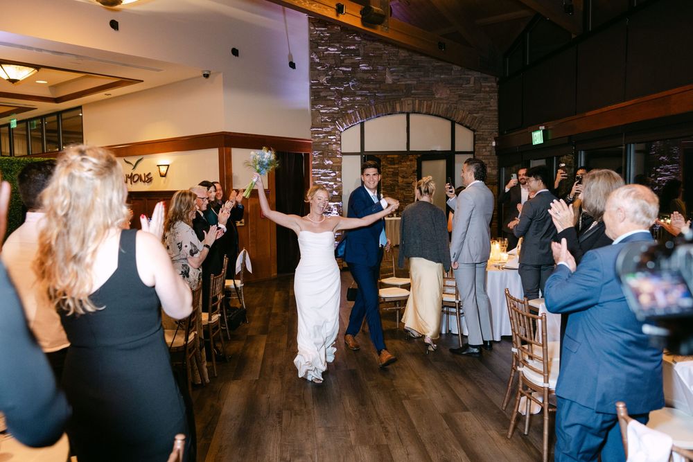 Large group of wedding attendees dancing together in a rustic venue with stone accent walls.