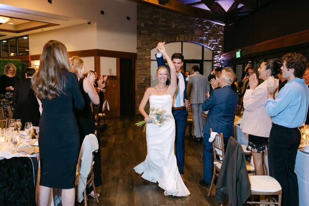 Wedding reception guests dancing and mingling in a rustic indoor venue with warm lighting.