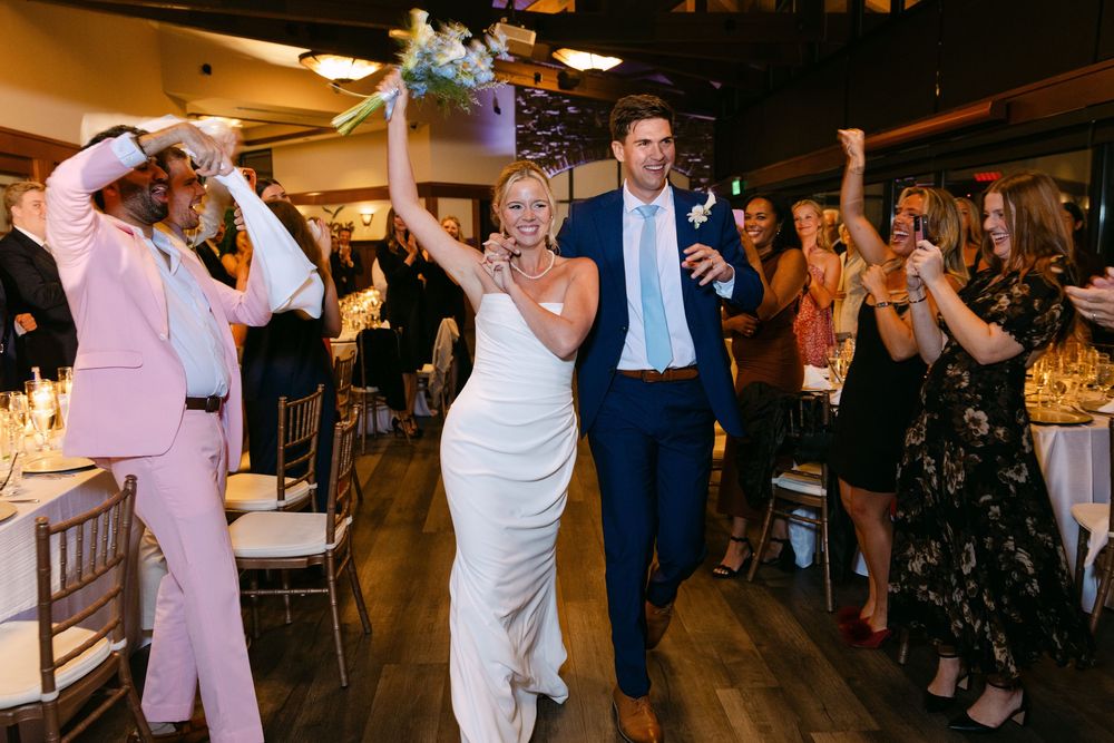 Wedding party dancing and celebrating in a dimly lit reception venue with wooden accents.