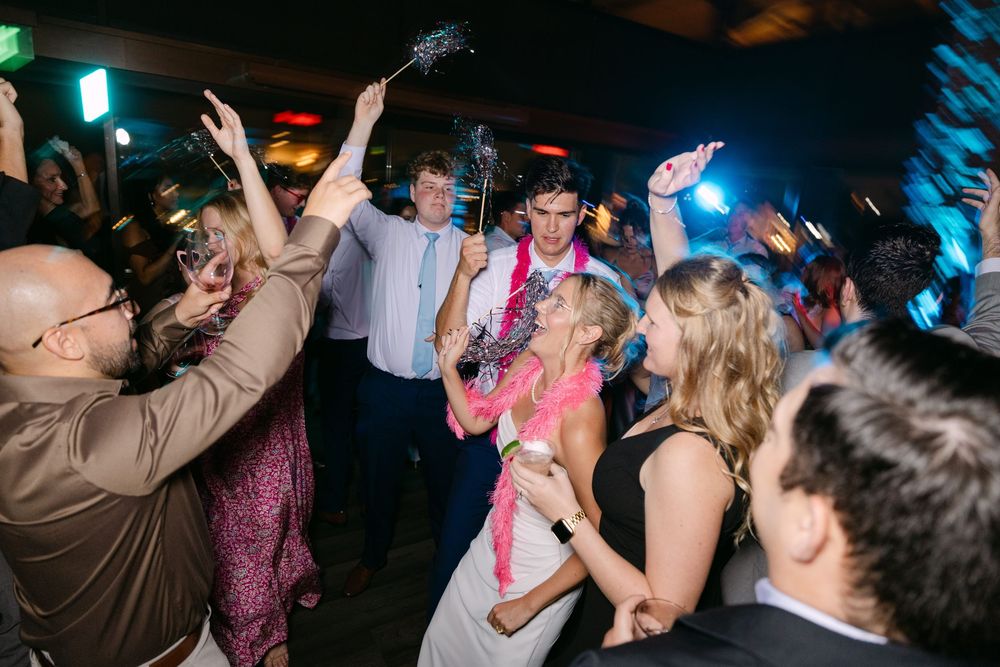 Guests dance and celebrate on a dimly lit dance floor with colorful lights creating a festive party atmosphere.