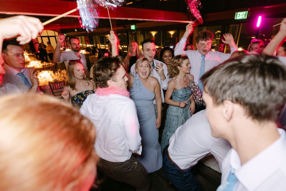 Wedding guests dancing and celebrating on a colorful illuminated dance floor at an indoor reception venue.