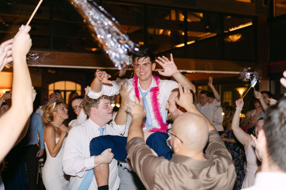 A group of people dancing and celebrating at a lively party or reception with dimmed lighting.