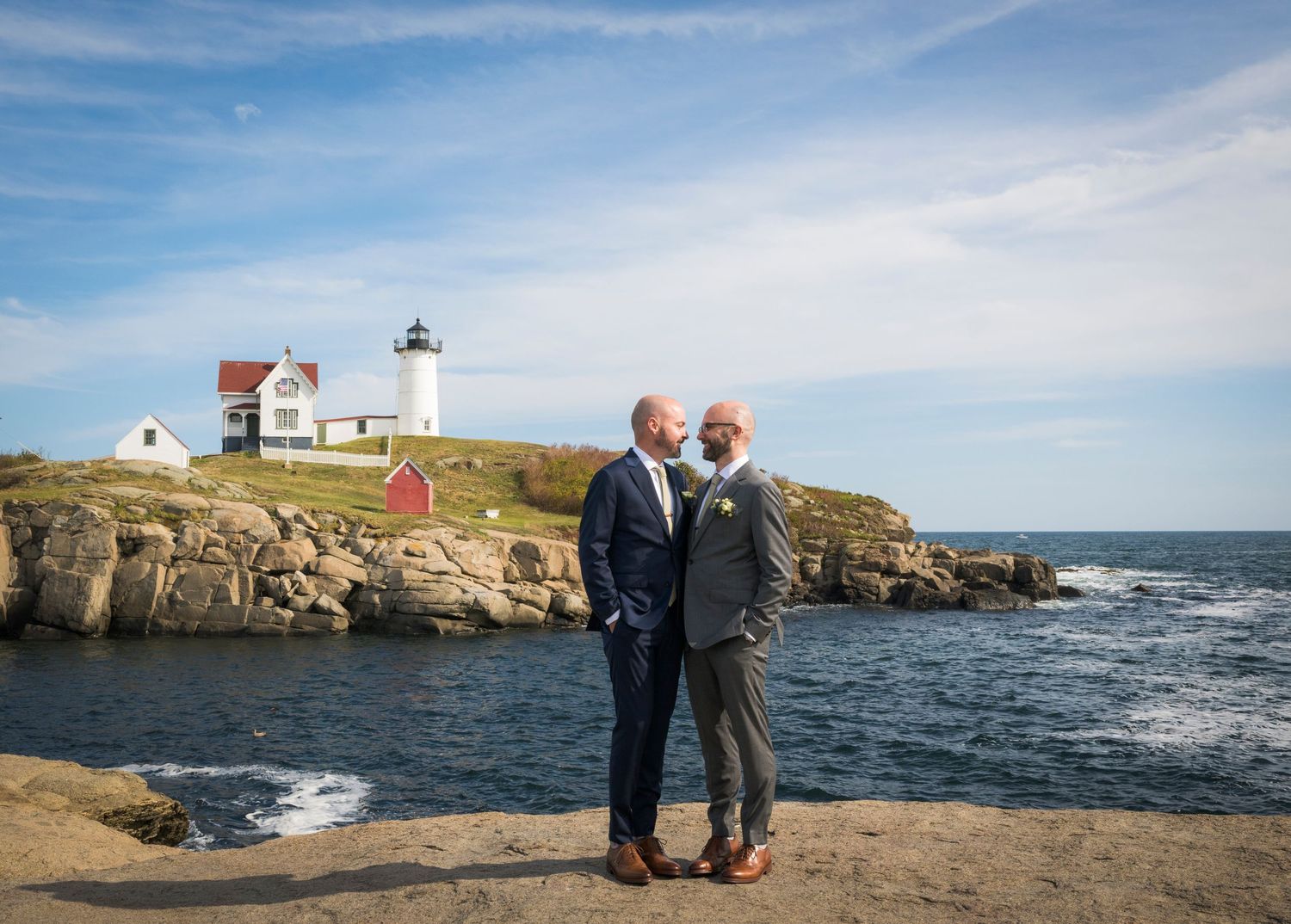 A romantic coastal engagement photo session at Nubble Lighthouse in Maine with dramatic ocean views and rocky cliffs.
