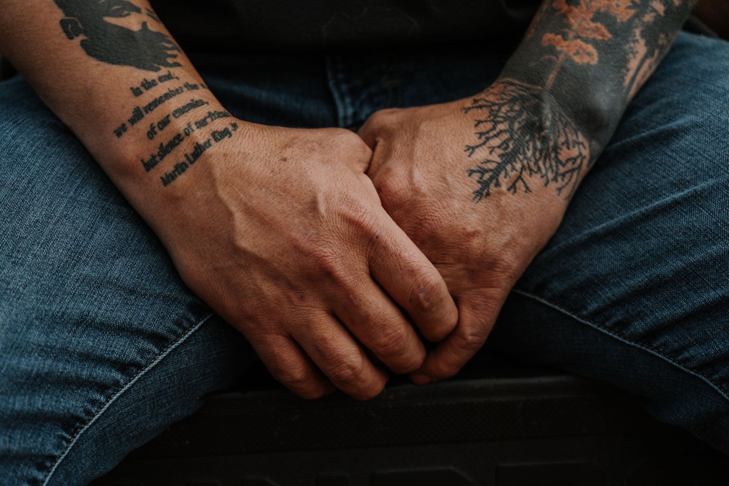 Close-up view of hands with tattoos resting on denim jeans in natural lighting.