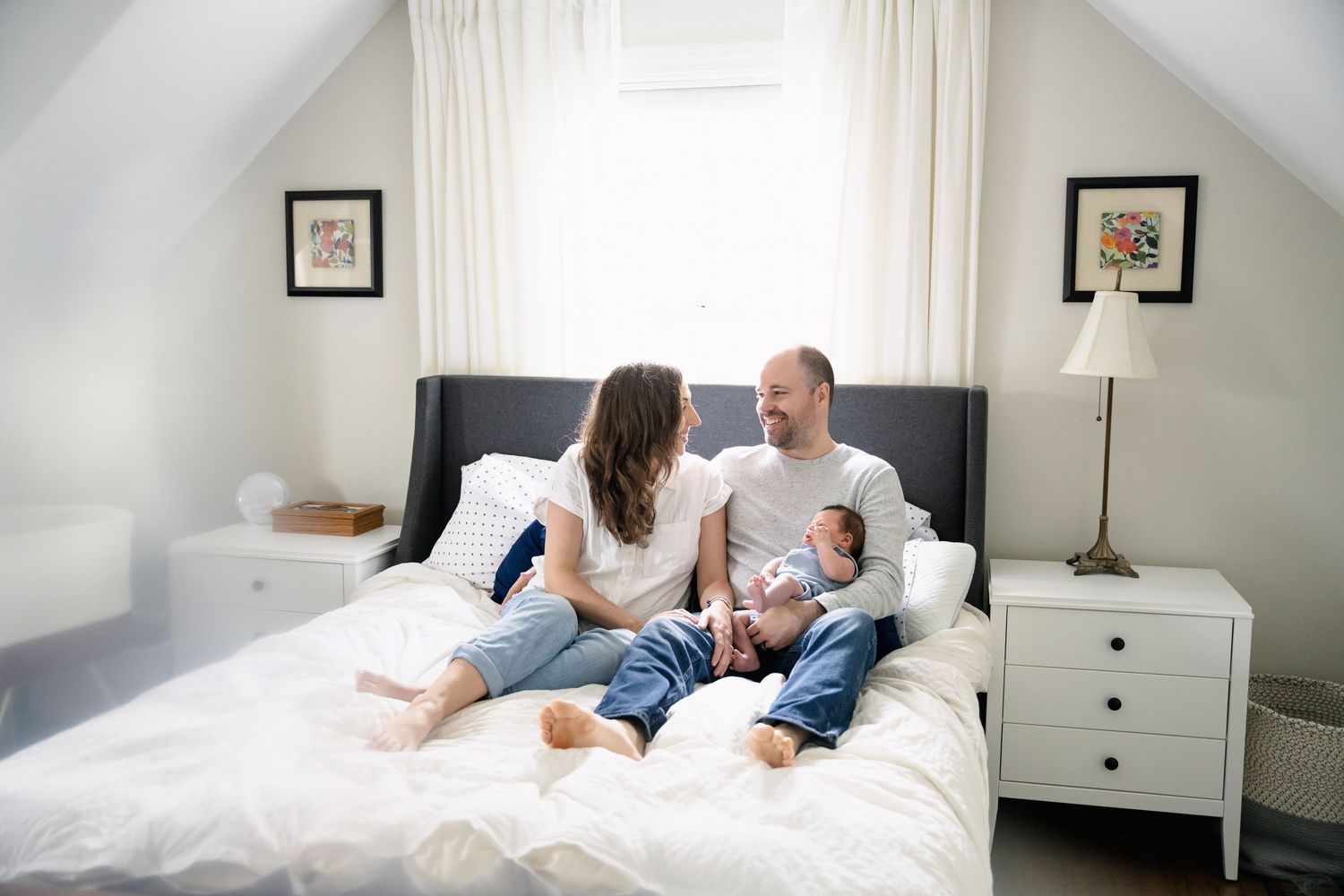 A family relaxes together on a white bed in a bright, minimalist bedroom with natural lighting during a family session in Mount Prospect
