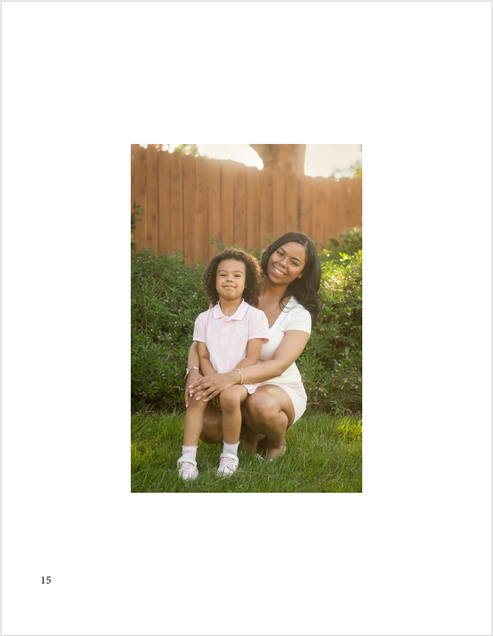 daughter sitting on mother's lap while crouched near grass and bushes