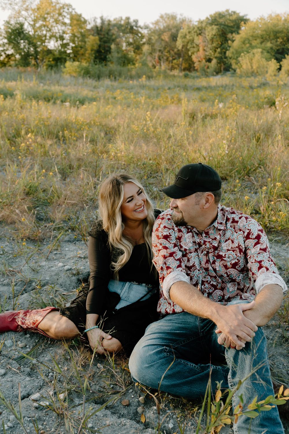 A couple shares tender moments while laying in a grassy field during golden hour.