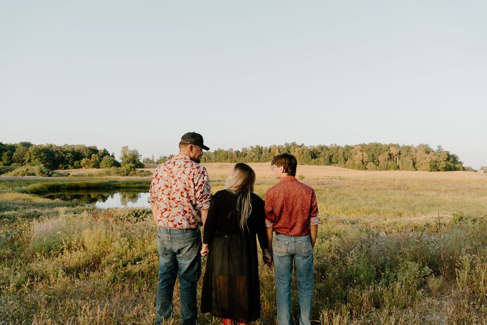 Three people stand together looking out across a golden field at sunset in a warm autumn landscape.