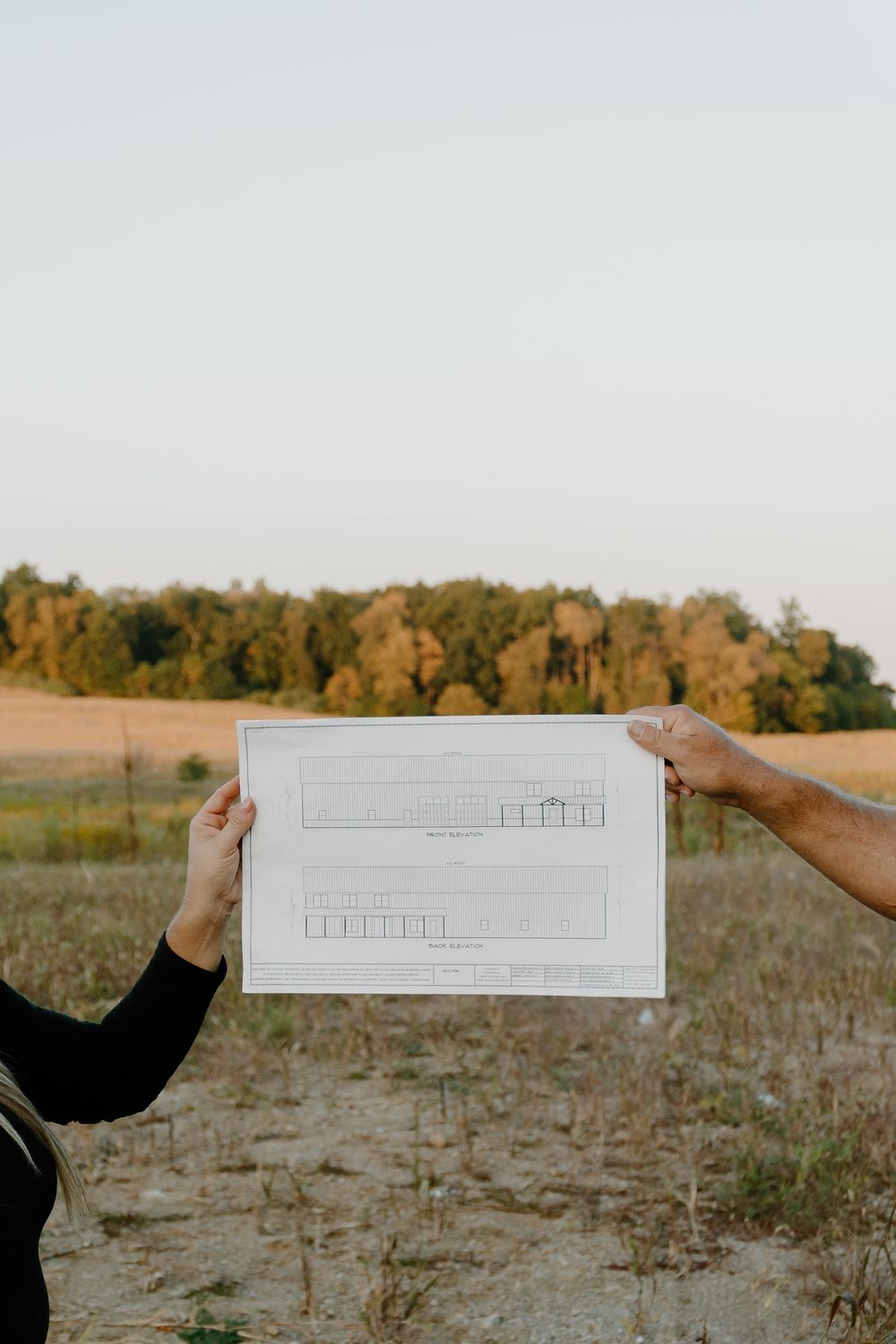 A sequence of hands holding architectural drawings against a golden autumn field at sunset.