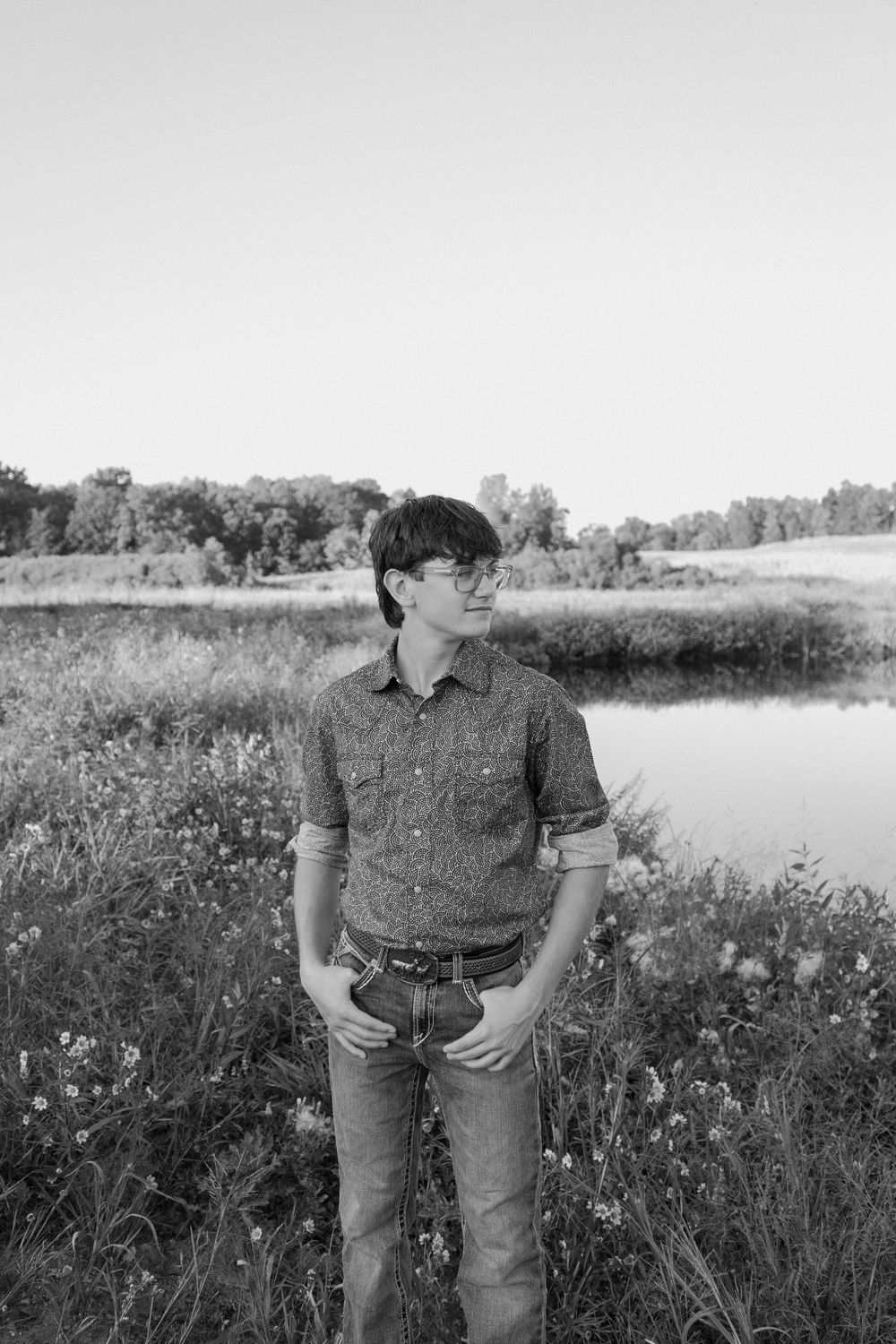 A person in casual attire stands in a field of wildflowers beside a pond during golden hour.