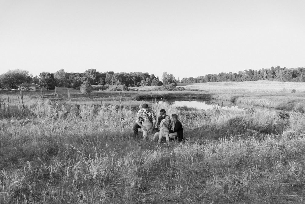A black and white panoramic photograph shows people sitting in a grassy field on a sunny day.