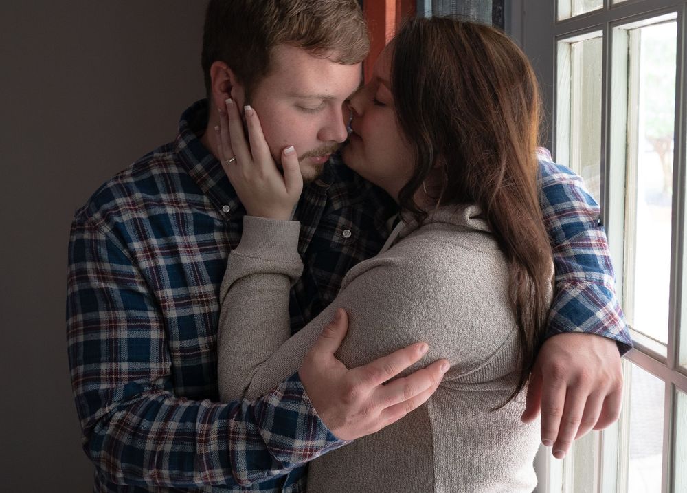 A couple in plaid and grey clothing share an intimate moment by a window in a sequence of three photos.