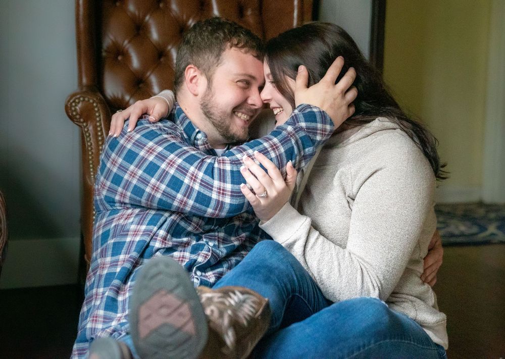 A couple shares a tender moment while sitting together on a couch in a casual home setting.