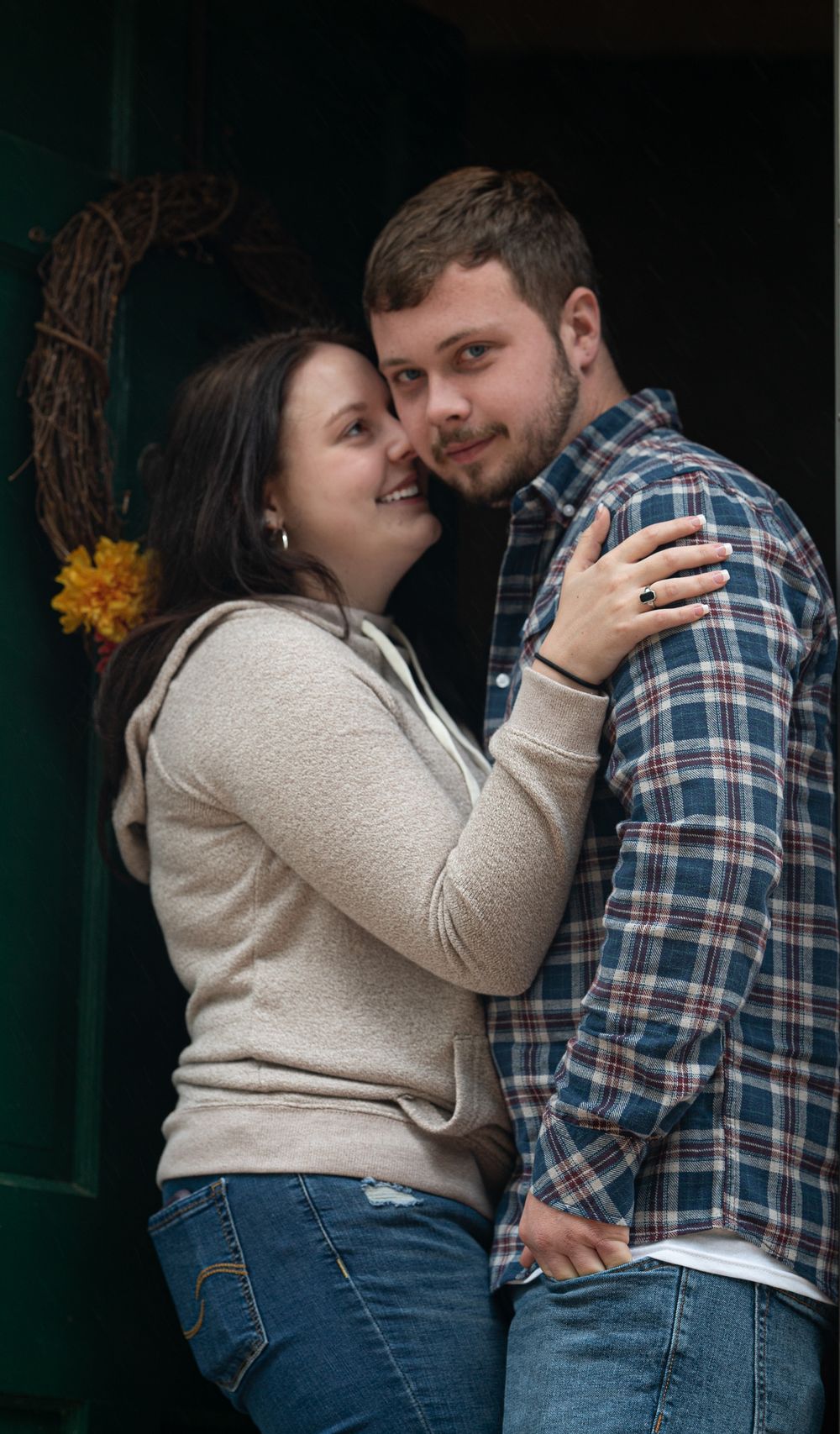 A couple embraces tenderly in a romantic photoshoot wearing coordinating plaid and cream sweater outfits.