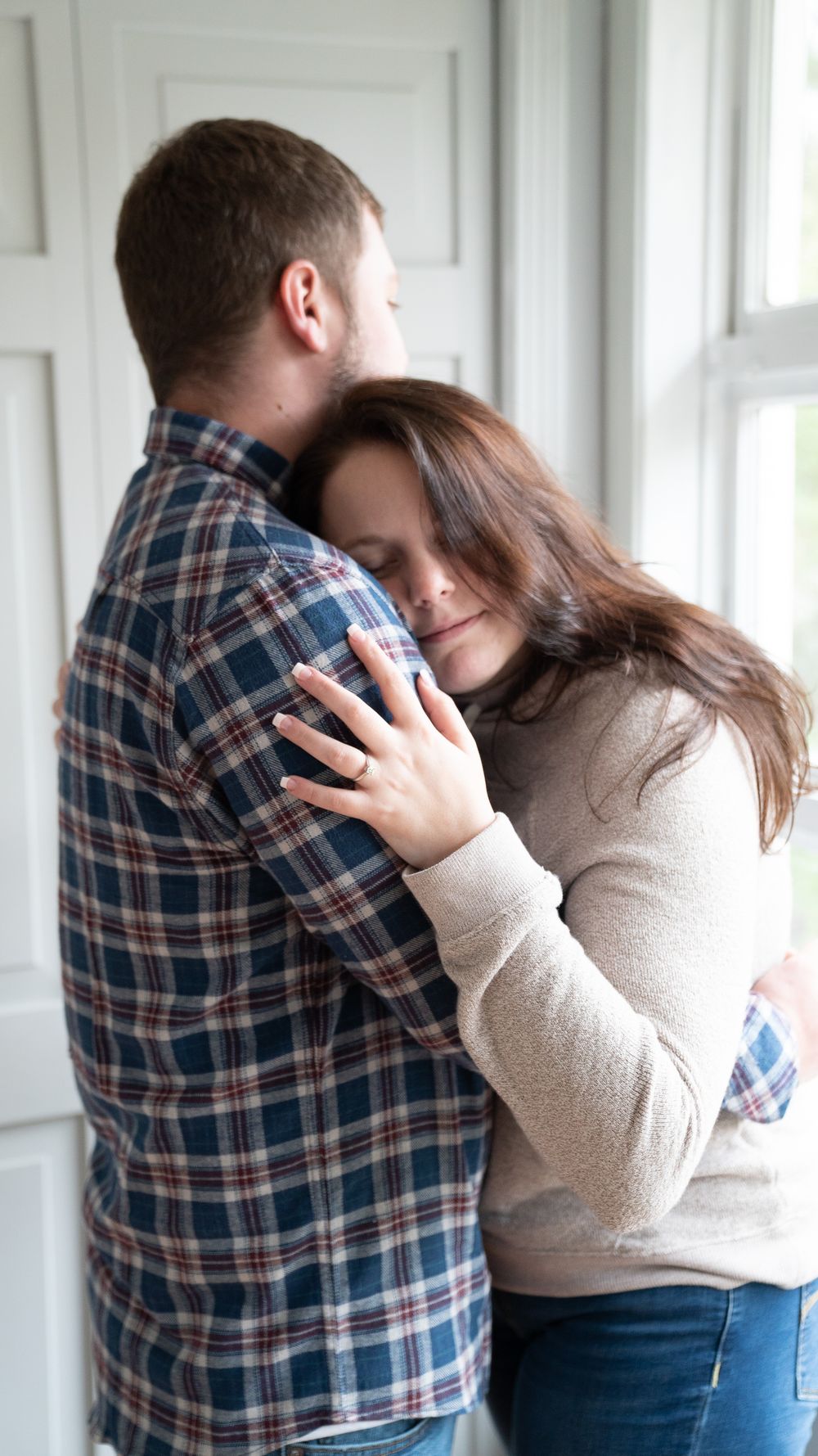 A couple embraces in a romantic sequence of photos showing tender affection near bright windows.