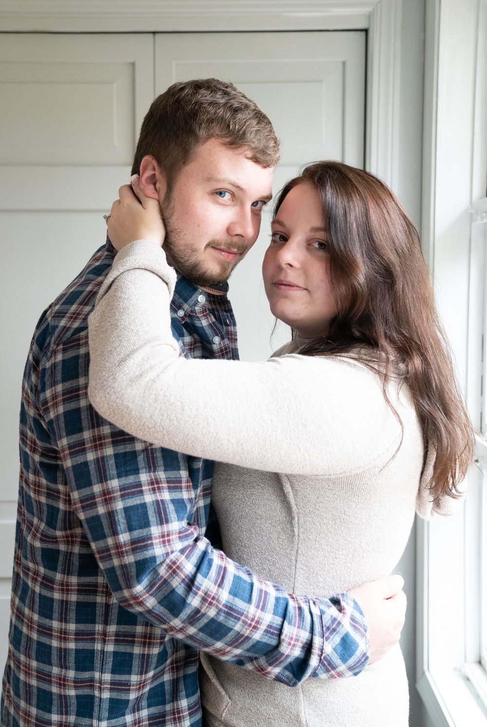 A couple in casual attire embraces near a window in a series of romantic poses.
