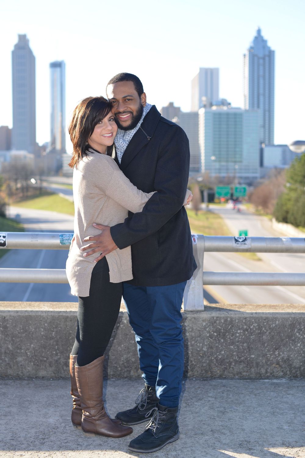 A couple shares a romantic moment against the Atlanta skyline backdrop on a sunny winter day.