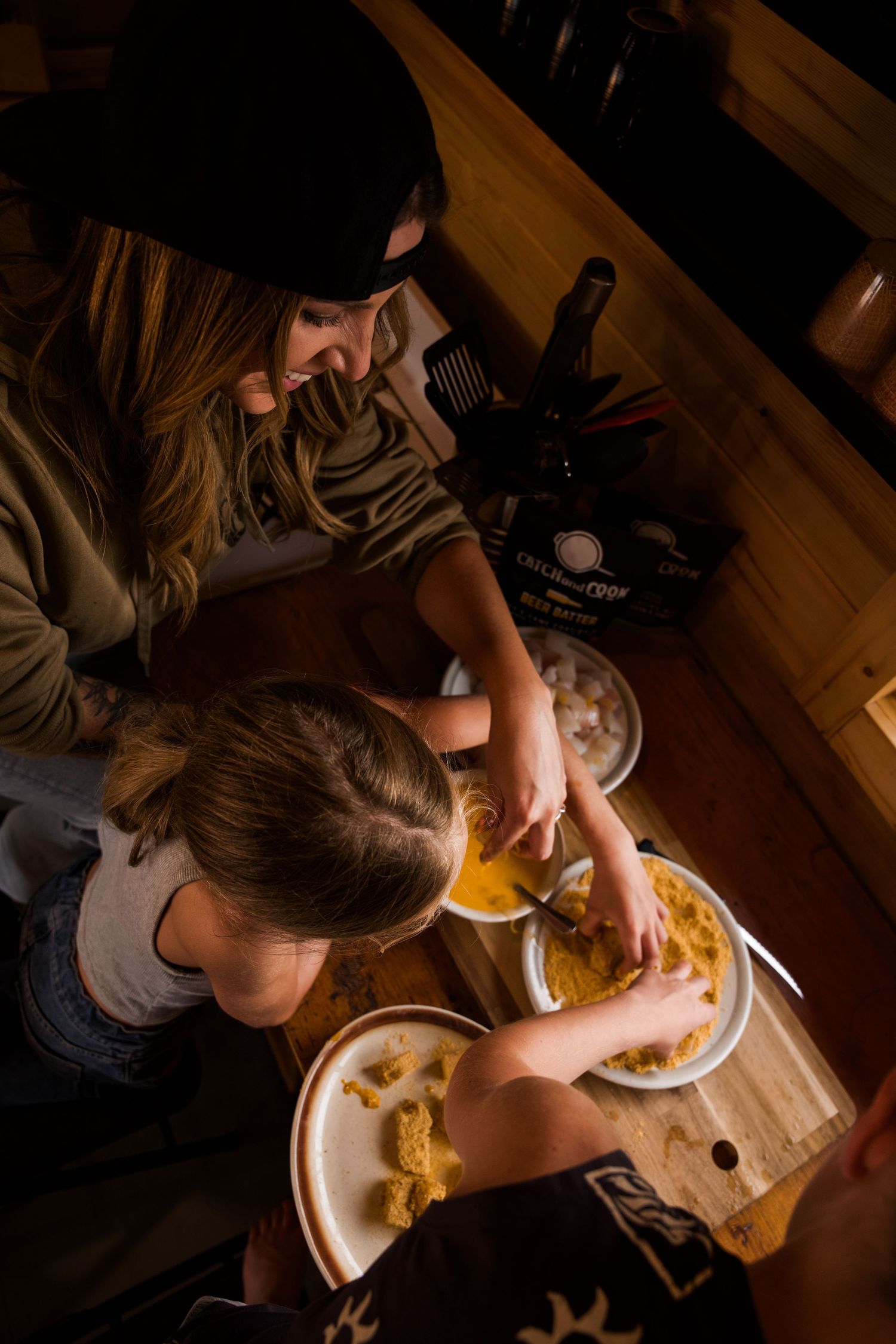 Overhead view of people preparing and eating food at a wooden dining table.